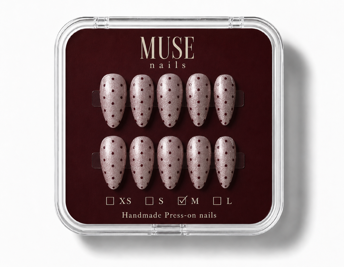 A set of ten premium press-on nails by Muse nails, The nails have a light pinkish-beige base with burgundy polka dots