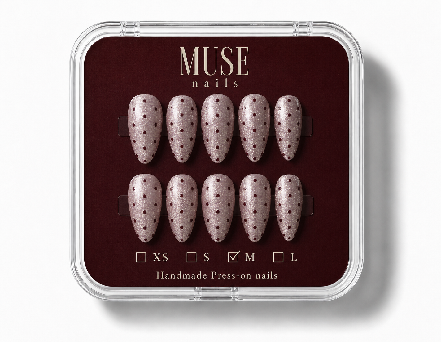 A set of ten premium press-on nails by Muse nails, The nails have a light pinkish-beige base with burgundy polka dots