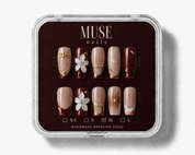 A set of 10 press-on nails. The nails feature a mix of nude beige and deep burgundy with gold foil details, white floral accents, and star motifs.