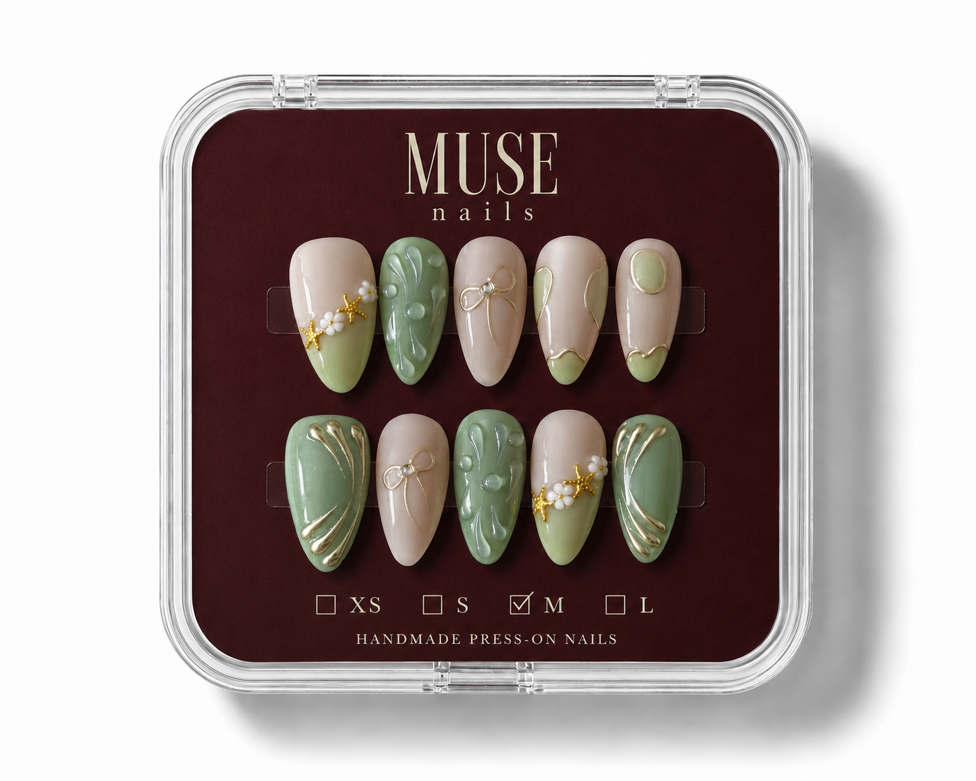 MUSE nails press-on set in a clear plastic clamshell case with a dark burgundy insert. The set features almond-shaped nails in beige and sage green with gold leaf and floral details, with size options XS, S, M, and L indicated.