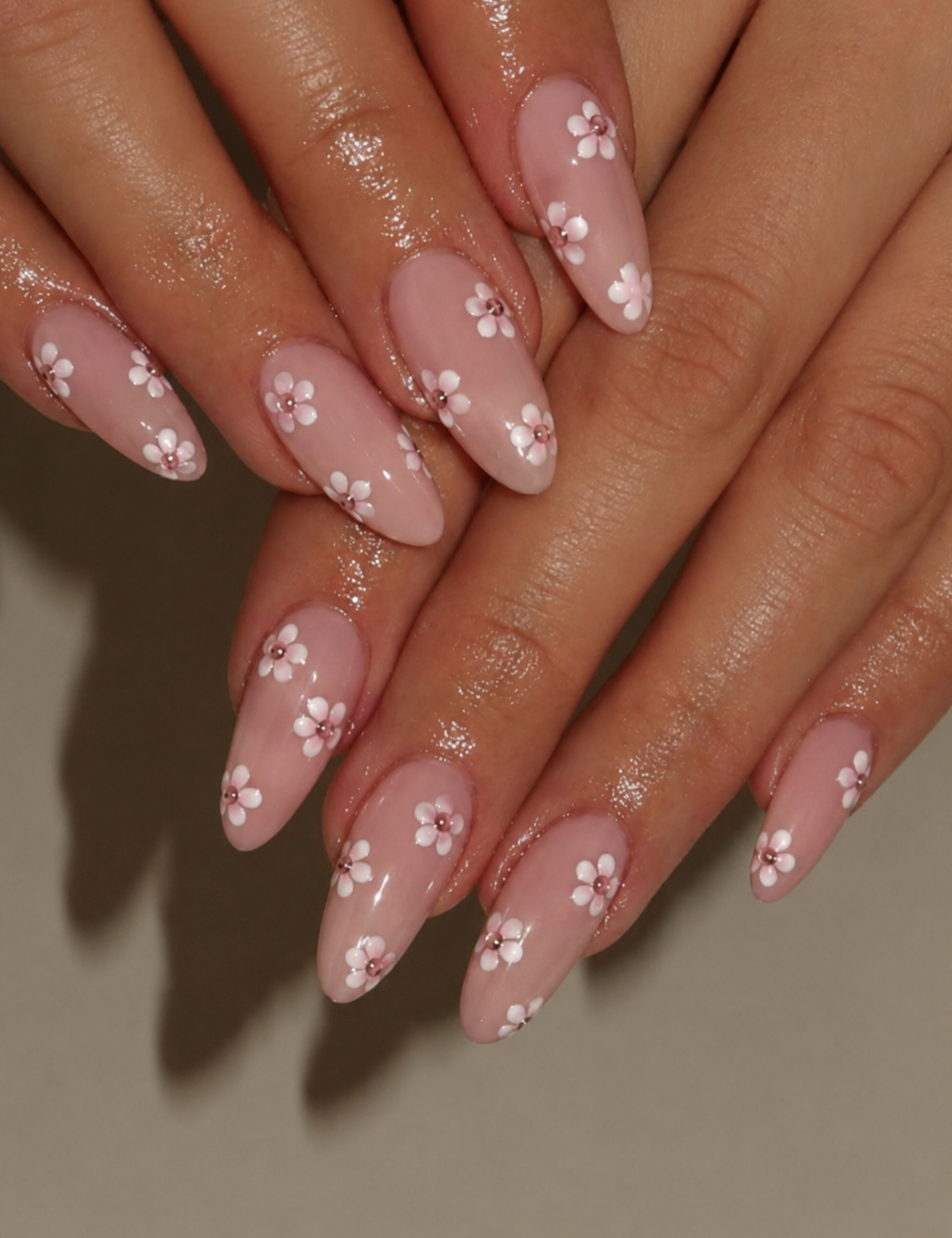 Close-up of manicured fingering with long almond-shaped nails painted in a glossy dusty pink base and decorated with small white cherry blossom flowers.