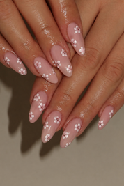Close-up of manicured fingering with long almond-shaped nails painted in a glossy dusty pink base and decorated with small white cherry blossom flowers.