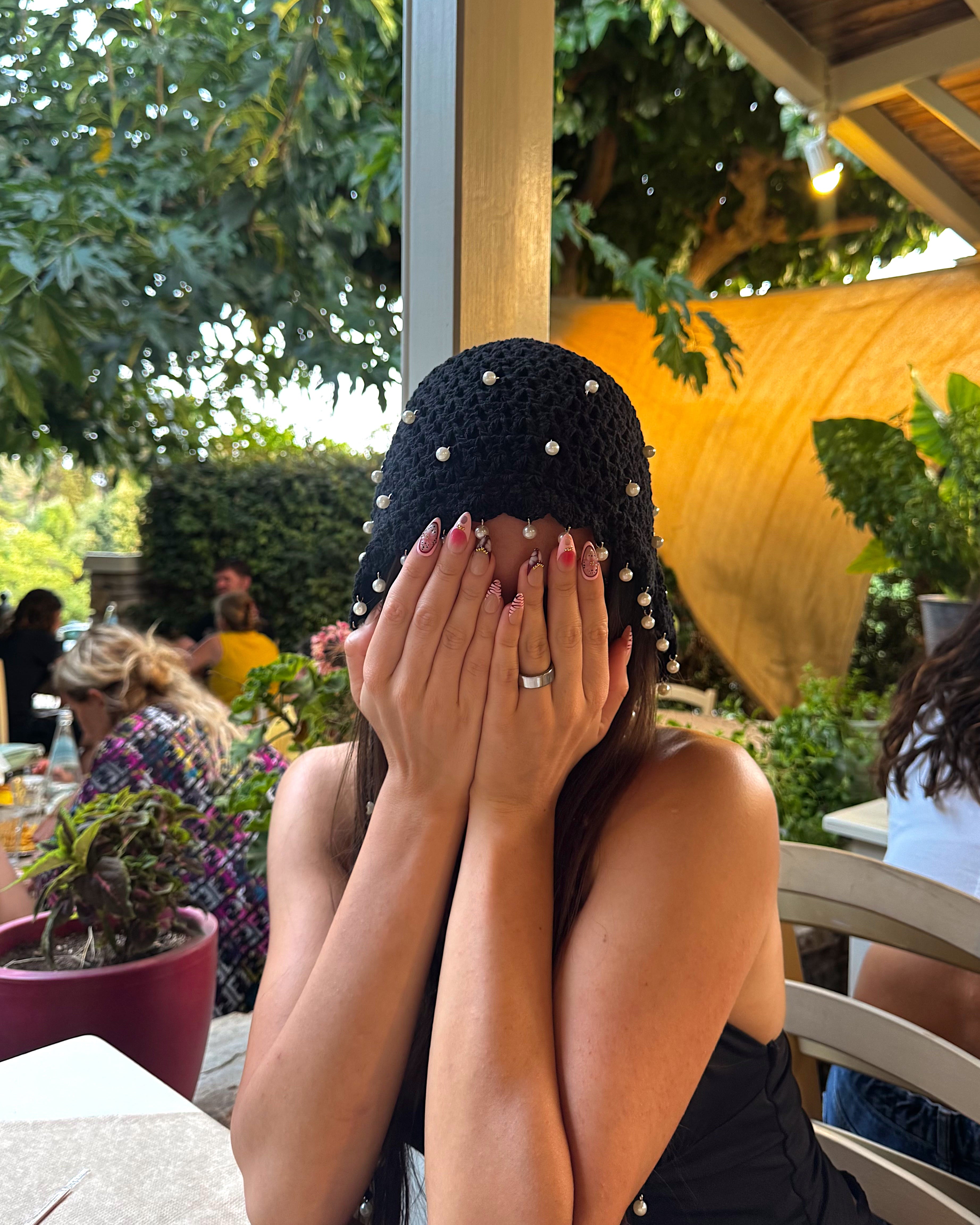A woman sitting at an outdoor patio table with pink floral motif nails nail art
