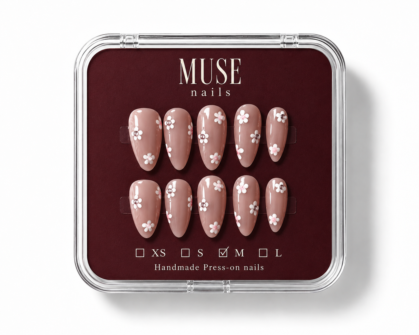 A set of 10 press-on nails by MUSE nails, displayed in a clear plastic clamshell case with a dark burgundy insert. The nails are a warm nude pink with white floral patterns, and the size 'M' is checked on the size guide at the bottom.